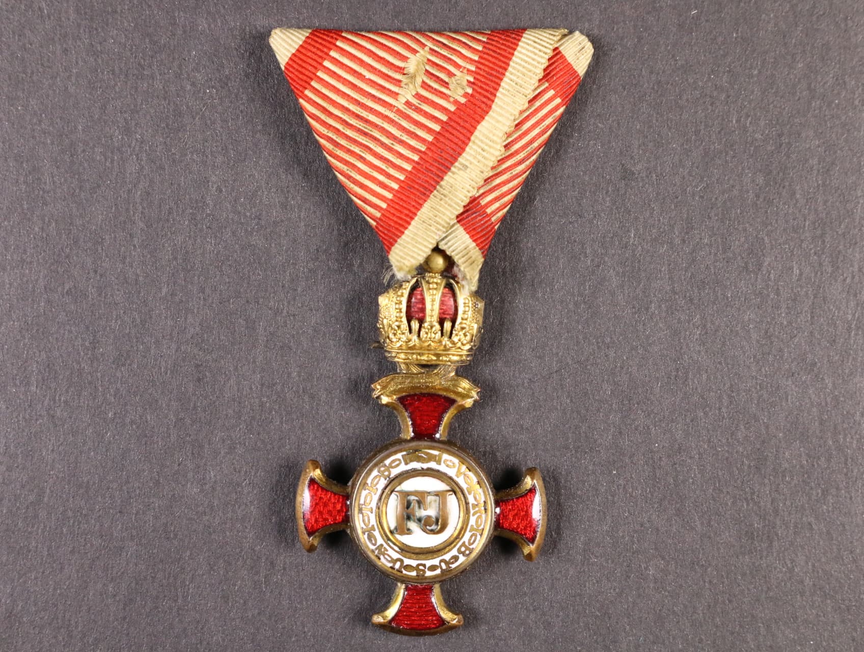 Zlatý záslužný kříž s korunou, na závěsném kroužku hvězdička a značka výrobce Wilh. Kunz Wiwn, pozlacený bronz, na spodním rameni na reversu vypadený smalt