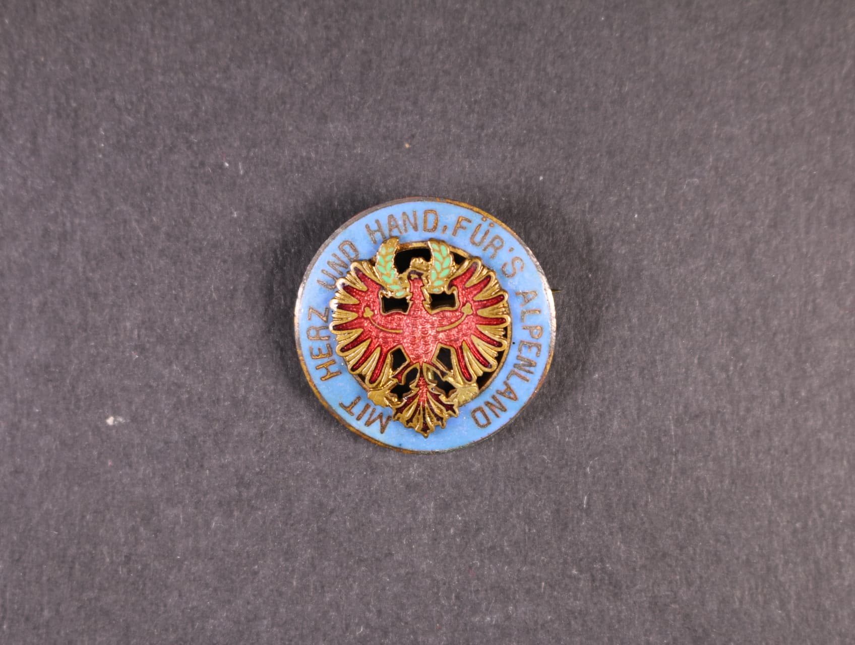 Patriotický odznak, Tyrolská orlice rámovaná modře smaltovaným kruhem s nápisem, MIT HERZ UND HAND FuR´S ALPENLAND, upínání na vodorovnou jehlu, zlacený bronz, smalty